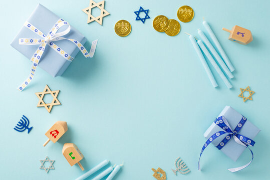 Festival of Lights: Overhead image featuring Star of David, menorah signs, gelt, trendy gift boxes, candles and dreidel on a pastel blue background, circular space perfect for text or advertising