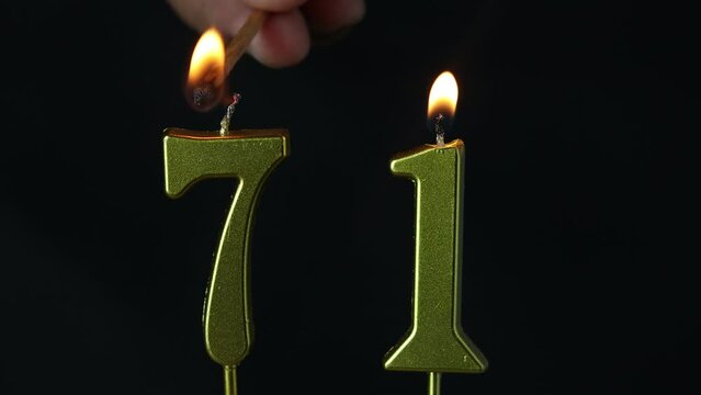 close up on the gold number seventy-first candle on a dark background.
