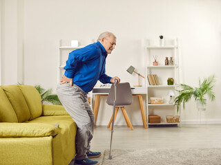 Senior man suffering from back pain at home. Elderly man with walking cane feeling pain while trying to get up from couch. Old age, medical and healthcare concept
