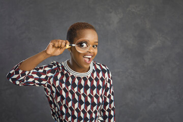 Studio shot of happy black woman with magnifying glass looking at you with funny big eye. Young...