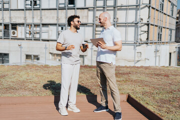 Two professionals collaborate outdoors, analyzing a construction project. They discuss blueprints,...