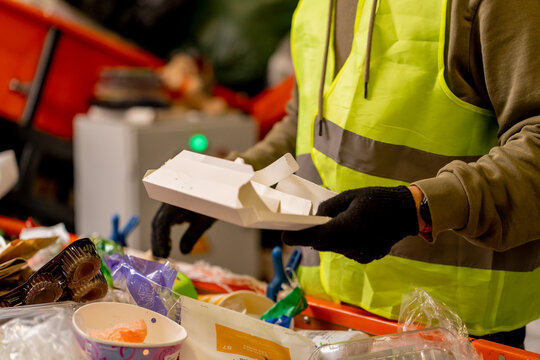 Hands in gloves of a uniformed employee sort garbage into categories on a special line at waste recycling plant