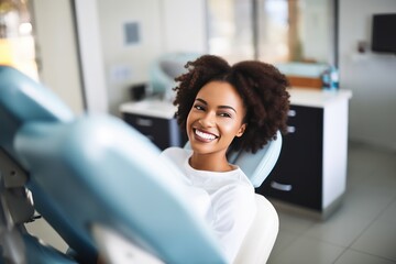 Close-up photo of a smiling African American woman sitting in a chair in a dental office. She is waiting for the dentist for an oral procedure. Teeth whitening concept. - obrazy, fototapety, plakaty