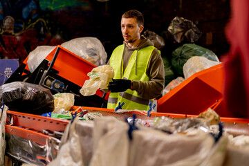 An employee in a uniform and gloves at a waste recycling station sorts and sorts garbage on sorting...