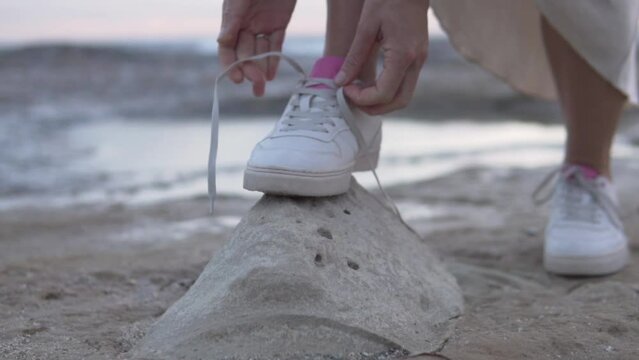 Close-up, a woman tying a shoelace on her sneakers on a stone by the sea