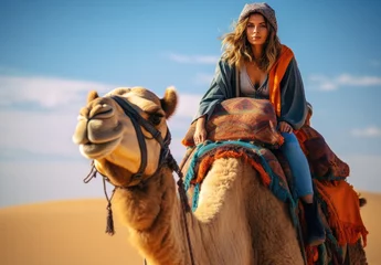 Fotobehang In the desert, a happy traveler riding a camel enjoys an adventurous and exotic journey. © Iryna