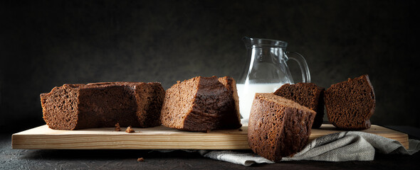 Chocolate donut, ciambellone with milk carafe and cutting board on dark background, closeup, space for text.