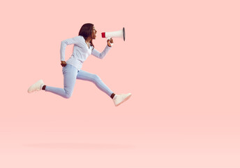 African American woman running and jumping making announcement through megaphone. Profile view of woman with loudspeaker isolated on pastel pink background. Concept of marketing, sales and discounts.