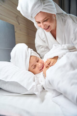 Attractive mother in bathrobe tickling her pretty little daughter