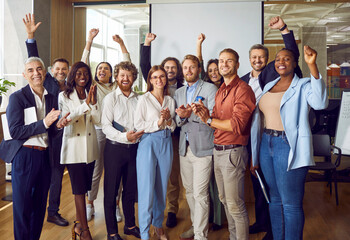 Portrait of diverse excited happy business people standing in office applauding and looking cheerful at the camera. Group of coworkers men and women smiling indoors. Team work concept. - Powered by Adobe