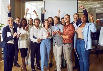 Poster Portrait of diverse excited happy business people standing in office applauding and looking cheerful at the camera. Group of coworkers men and women smiling indoors. Team work concept. © Studio Romantic
