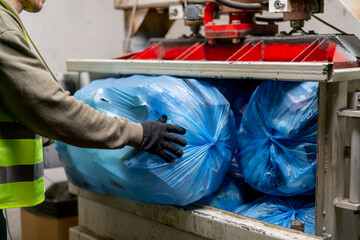 Close-up shot of male hands in gloves loading large garbage bags into special garbage compactor...