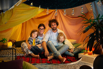 Obraz na płótnie Canvas Amazing family time spending two cute and pretty boys and their parents sitting on the floor inside the handmade tent in the kids room eating popcorn and watching a movie on the laptop