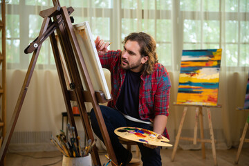 A painter is wearing a very colorful blue set of headphones and listening to music while he paints...