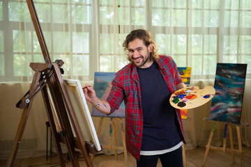 A young handsome working man is painting up a very nice canvas in his dazzling bright art studio