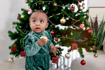 Portrait of adorable African little girl child with beautiful decorated Christmas tree in living room. Lovely cute kid celebrating winter holiday. Merry Christmas and Happy New year concept.