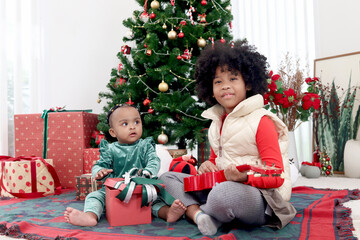 African child sister celebrate winter holiday together, little cute girl kid and curly hair sibling feel excited about Christmas present gift box under beautiful Christmas tree, happy childhood family