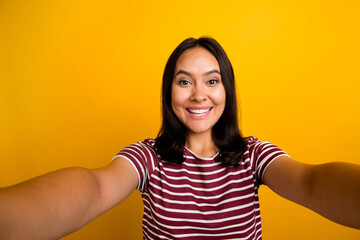 Portrait of toothy beaming optimistic woman with straight hairdo dressed stylish t-shirt making selfie isolated on yellow background