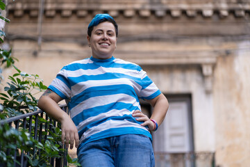 A genderfluid individual with blue short hair and a nose piercing smiles at the camera in a natural...