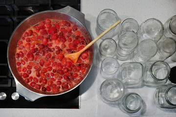 Cooking strawberry jam in a large bowl at home. Wooden spoon in a bowl with jam.Empty glass jars for jam.
