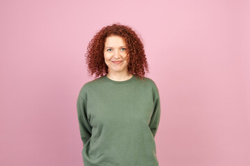 Studio portrait of cute smiling shy redhead female with curly hair in green sweatshirt with copy...