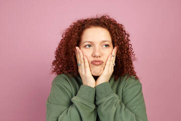 Studio portrait of pretty bored funny ginger head millennial girl with cute curls touching her...