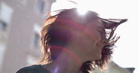 Carefree woman shaking hair outside in the sunlight with flare adult girl shakes head sideways
