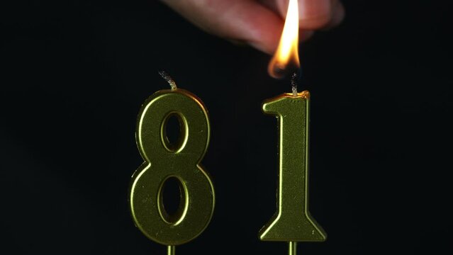 close up on the gold number eighty-first candle on a dark background.

