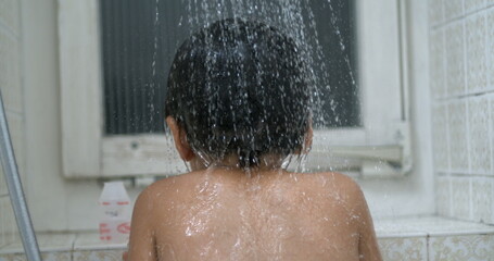 Back of child with water flower in super ultra bathing kid underneath shower head