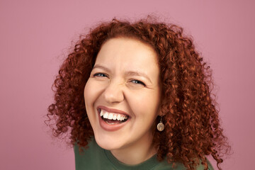 Studio headshot of cheerful laughing woman with red curls, demonstrating white teeth, isolated...