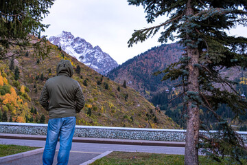 Fototapeta na wymiar Autumn landscape in the mountains, view from the dam to the mountains and the cable car near Almaty. View from the dam to the mountains. A man in autumn clothes looks into the distance at the mountain