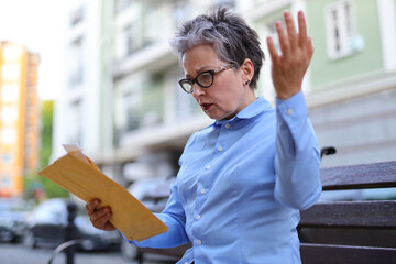 A mature female entrepreneur, deeply engrossed in her work outdoors, wrestling with pressing...