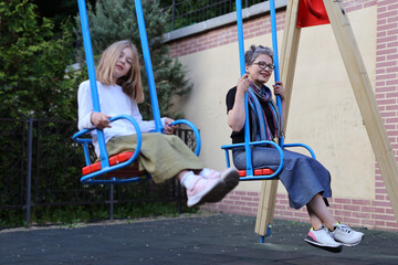 "Young girl and mature woman, sharing a joyous moment on a swing in a sunny playground."