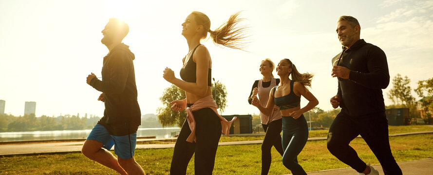 Group of happy sporty friends having outdoor workout in summer. Diverse multiethnic people in sportswear running together on city streets against bright sunny skies. Sport concept banner background