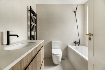 Fully tiled bathroom with beige stone tile, wooden furniture under the sink, black taps and...