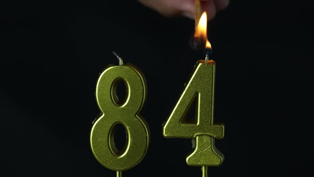 close up on the gold number eighty-fourth candle on a dark background.
