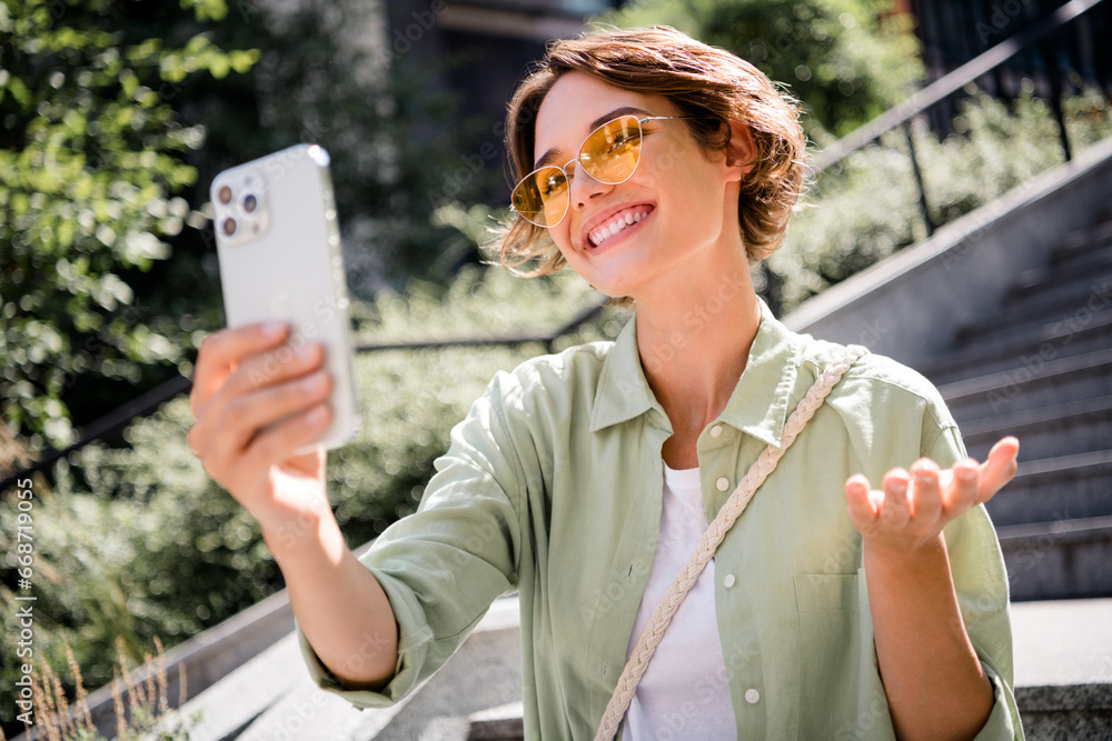 Poster Photo of positive lovely friendly girl blogger wearing stylish shirt sitting on stairs outdoors telling news weekend sunny day