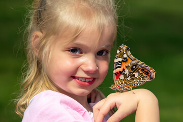 girl with a butterfly. a little girl with a tail on her head holds a large bright butterfly on her hand, the butterfly sits on the girl’s hand