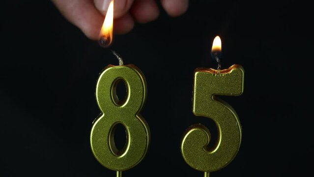 close up on the gold number eighty-fifth candle on a dark background.

