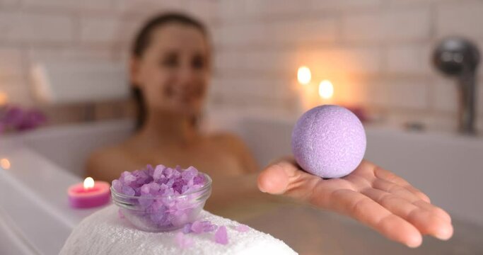 woman relaxing in bathtub in candle light and holding bath bomb in hand for body skin moisturizing. home spa, skincare