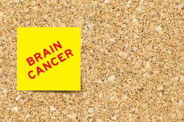 Yellow note paper with word brain cancer on cork board background with copy space