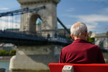 Fototapeta premium Budapest, Hungary - October 1, 2023: A senior tourist with Szechenyi Chain Bridge and Buda Castle in the background. Széchenyi lánchíd, Budavári Palota