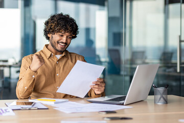 Portrait of young successful hispanic businessman financier, man smiling contentedly, holding hand up celebrating victory, and successful achievement results, investor paperwork.