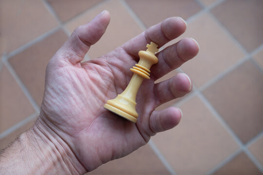 La pieza de ajedrez el rey blanco en la mano de un jugador con fondo ajedrezado.