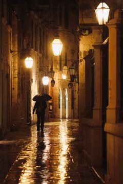Person walking in the rain at night. Man with an umbrella. Old historical street with warm lamps. 