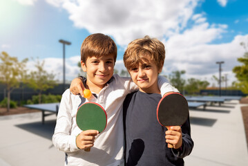 Two kids with ping pong paddles playing at outdoor sports facilities. Sportsmanship in youth. After-school activities for children