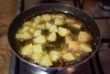 Selective focus on a frying pan cooking French fries. Frying golden potatoes in hot oil on the stovetop