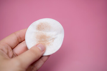Girl holding a cotton pad in her hand, sponge for removing make-up, on pink background. Foundation cream. © leroy