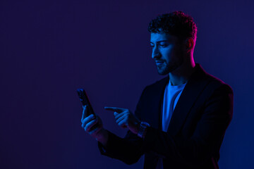 Man with phone in hand looking at smartphone screen, portrait dark blue background, neon light.