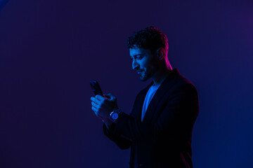 Man with phone in hand looking at smartphone screen, portrait dark blue background, neon light.